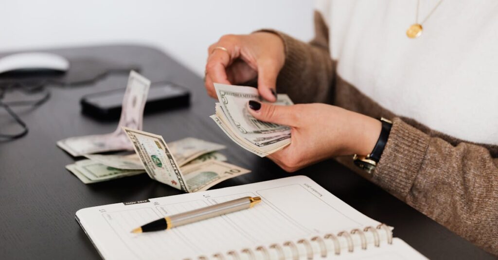 Close-up of person counting cash with notepad on desk, indicating financial tasks.