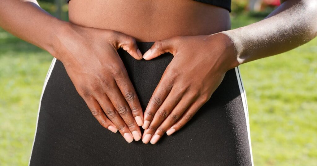 Close-up of hands forming a heart shape on woman's belly, symbolizing health and love.